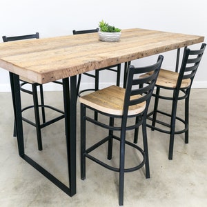 May include: A rustic wooden table with black metal legs and four black metal bar stools. The table top is made of reclaimed wood and has a natural finish. The stools have a simple design with a slatted back and a round seat.
