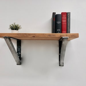 May include: A wooden shelf with metal brackets, holding a small potted plant and a stack of books. The books are titled "The Testament", "Breaking Dawn", "The Historian", and "Better: A Letter to My Younger Self".