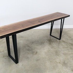May include: A long, dark brown wooden console table with a live edge top and black metal hairpin legs.