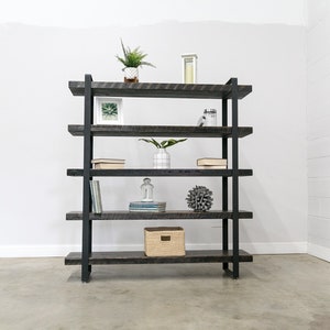 May include: A rustic, four-shelf bookcase with a dark gray finish and black metal frame. The shelves are filled with decorative items like plants, books, and a woven basket. The bookcase is approximately 60 inches tall and 48 inches wide.