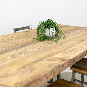 May include: A rustic wooden dining table with a natural wood finish. The table has a live edge and is made of reclaimed wood. The table is surrounded by metal chairs with wooden seats.