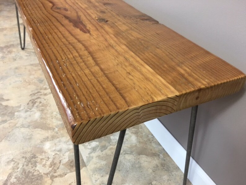 K&ouml;nnte beinhalten: Eine Holzbank mit nat&uuml;rlicher Holzoptik und Haarnadelbeinen. Die Bank ist aus recyceltem Holz gefertigt und hat einen rustikalen Look.
