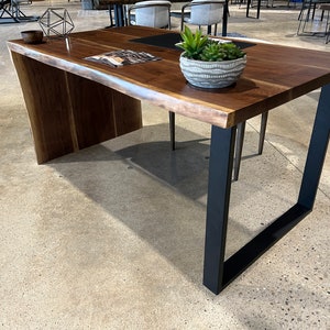 May include: A large, dark wood desk with a live edge top and black metal legs. The desk has a natural wood finish and a modern design.