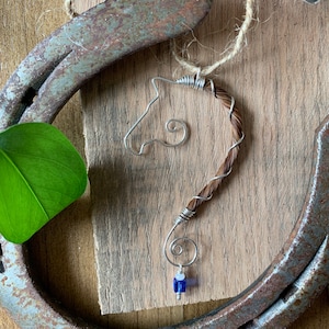 May include: A brown horsehair wrapped wire ornament in the shape of a horse's head with a blue glass bead at the bottom.
