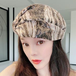 May include: A sequined beret in shades of brown and beige. The hat has a textured, patterned design and is worn on the head. The beret is a stylish accessory.