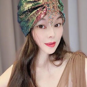 May include: A sequined turban in shades of green, gold, and pink. The head covering features a draped design and a beaded fringe. The turban is a glamorous accessory.