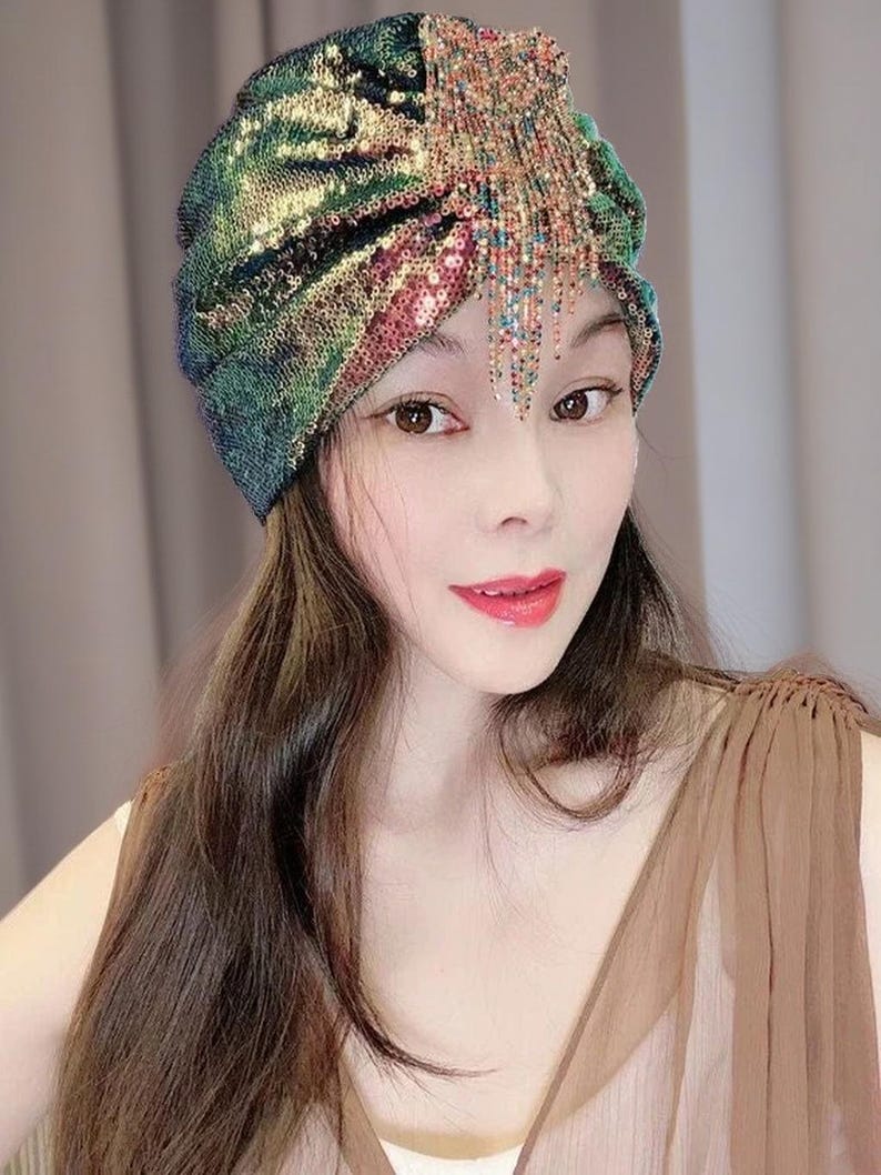 May include: A sequined turban in shades of green, gold, and pink. The head covering features a draped design and a beaded fringe. The turban is a glamorous accessory.