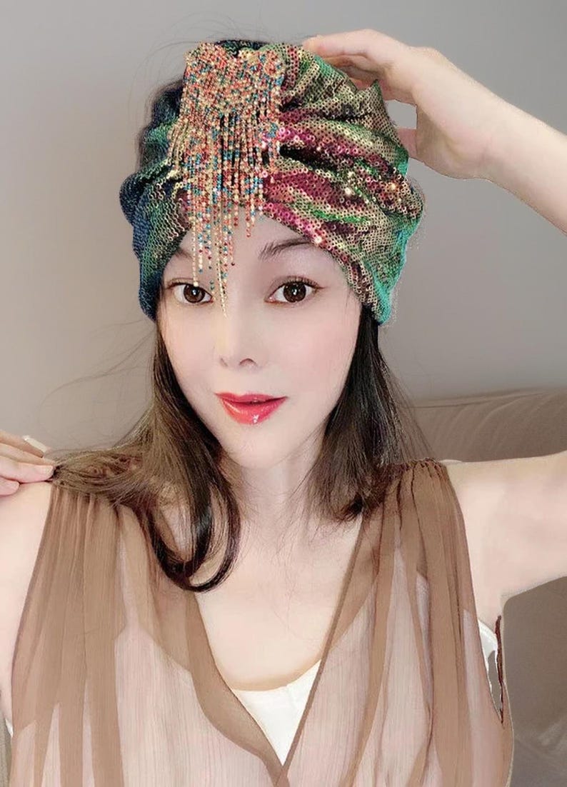 May include: A sequined turban in shades of green, blue, and pink, adorned with a beaded fringe. The head covering is a stylish accessory, perfect for adding a touch of glamour to any outfit.