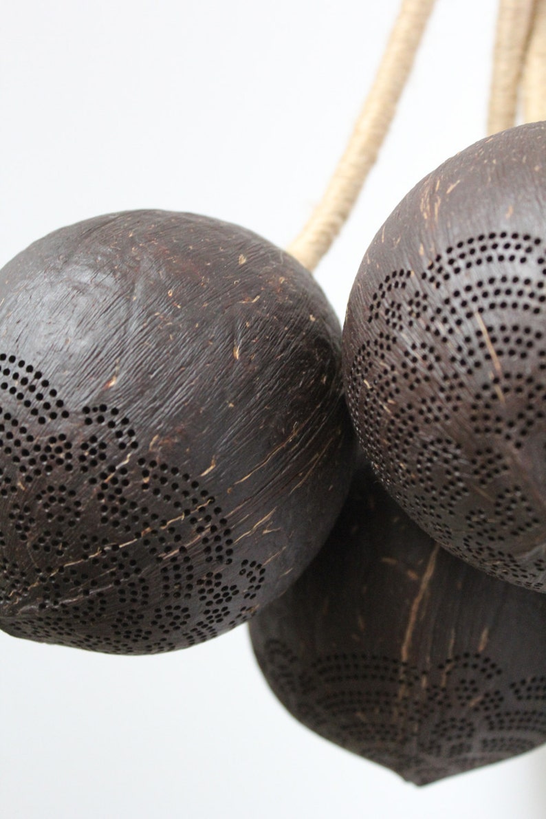 May include: Three brown coconut shell lanterns with intricate cut-out designs, hanging from a natural rope.