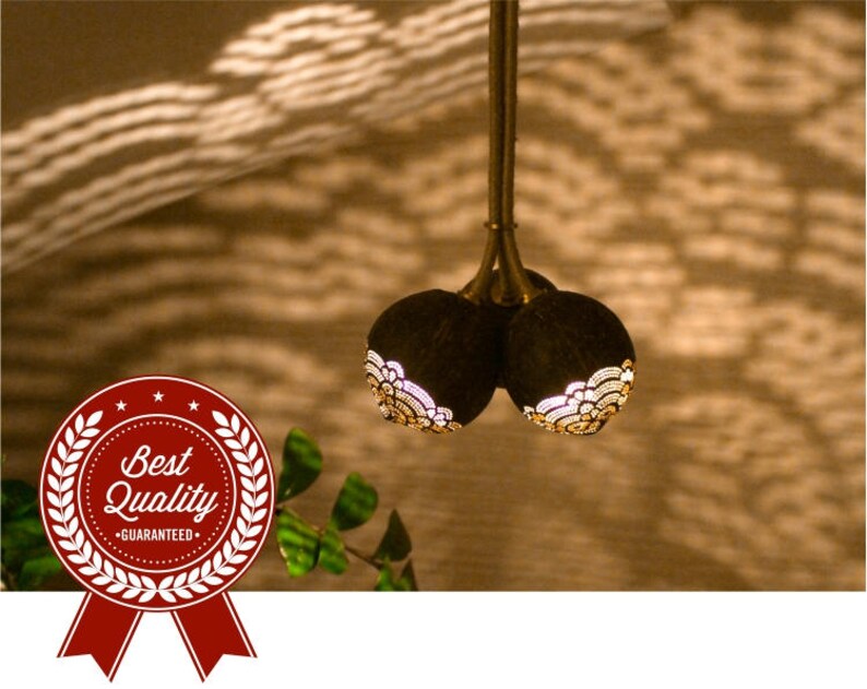 May include: A pendant light fixture made from two carved coconut shells with intricate designs. The shells are suspended from a gold-colored metal rod.