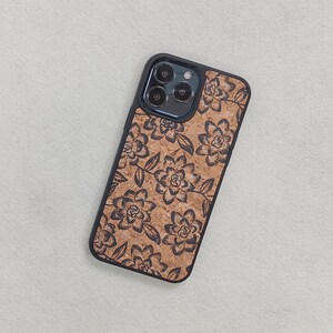 May include: A black phone case with a floral design. The case is made of cork and has a wood grain texture. The phone case has a cutout for the camera lens.