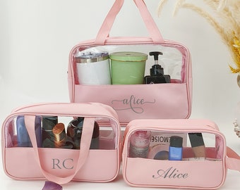 Puede incluir: Tres bolsas de viaje transparentes de color rosa con asas. La bolsa más grande tiene el nombre "alice" escrito en ella. La bolsa del medio tiene las iniciales "RC" en ella. La bolsa más pequeña tiene el nombre "Alice" escrito en ella.