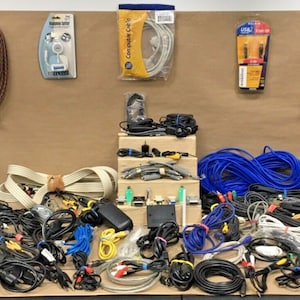 May include: A large collection of various types of cables and cords, including coaxial, RCA, HDMI, and Ethernet cables. There are also some power cords and adapters. The cables are arranged in a chaotic manner on a brown surface.