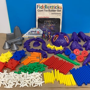 May include: A vintage Fiddlesticks Giant Toy Builder Set, featuring various colorful plastic pieces. The set includes purple, red, yellow, green, and blue components, along with a booklet. The set is designed for building and construction.
