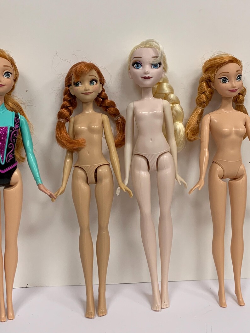 May include: Four plastic dolls standing in a row. The first doll on the left wears a turquoise and black leotard. The other three dolls are unclad, featuring molded skin-toned undergarments. Two dolls have auburn hair in braids, one has blonde hair in a side braid, and one has long auburn hair.