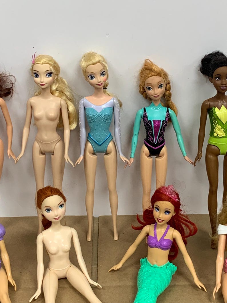 K&ouml;nnte beinhalten: Eine Sammlung von Modepuppen mit verschiedenen Hautt&ouml;nen und Frisuren. Einige Puppen tragen Badeanz&uuml;ge oder Kost&uuml;me, andere sind unbekleidet. Die Puppen haben bemalte Gesichtsz&uuml;ge und stehen in einer Gruppe.