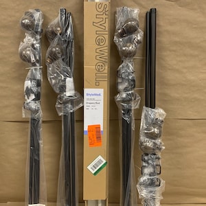 May include: Four black drapery rods and one white drapery rod in a cardboard box labeled StyleWell. The rods are wrapped in clear plastic and include decorative finials. The box displays the brand name StyleWell and product details.