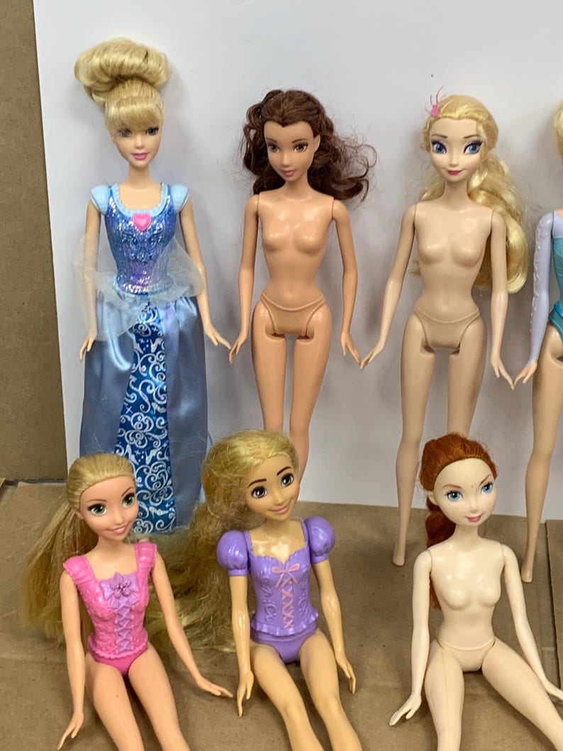 K&ouml;nnte beinhalten: Eine Sammlung von Modepuppen mit verschiedenen Charakteren. Eine Puppe tr&auml;gt ein blaues Kleid mit silbernem Oberteil und weitem Rock. Andere Puppen haben unterschiedliche Haarfarben und Outfits, darunter rosa, lila und blond.