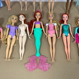 K&ouml;nnte beinhalten: Eine Sammlung von Modepuppen mit verschiedenen Outfits und Frisuren. Die Puppen sind in verschiedenen Posen und weisen eine Vielzahl von Farben auf, darunter Rosa, Lila, Gr&uuml;n und Blau. Einige Puppen haben lange Haare, andere k&uuml;rzere Stile.