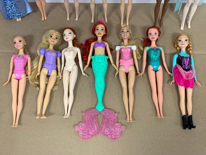 K&ouml;nnte beinhalten: Eine Sammlung von Modepuppen mit verschiedenen Outfits und Frisuren. Die Puppen sind in verschiedenen Posen und weisen eine Vielzahl von Farben auf, darunter Rosa, Lila, Gr&uuml;n und Blau. Einige Puppen haben lange Haare, andere k&uuml;rzere Stile.