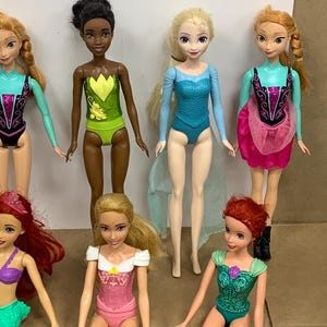K&ouml;nnte beinhalten: Eine Sammlung von Modepuppen mit verschiedenen Charakteren. Die Puppen tragen farbenfrohe Outfits, darunter Badeanz&uuml;ge und Kleider. Die Puppen haben lange Haare und sind in verschiedenen Posen dargestellt. Die Puppen sind aus Kunststoff und f&uuml;r Kinder konzipiert.