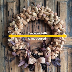 May include: A brown cork wreath with a burlap bow and black berries. The wreath is decorated with dried leaves and is approximately 18 inches in diameter. "How a wreath is measured" is written in yellow text across the center of the wreath.