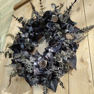 May include: A black and silver dried flower wreath with a variety of textures and shapes. The wreath is made with dried flowers, leaves, and branches.