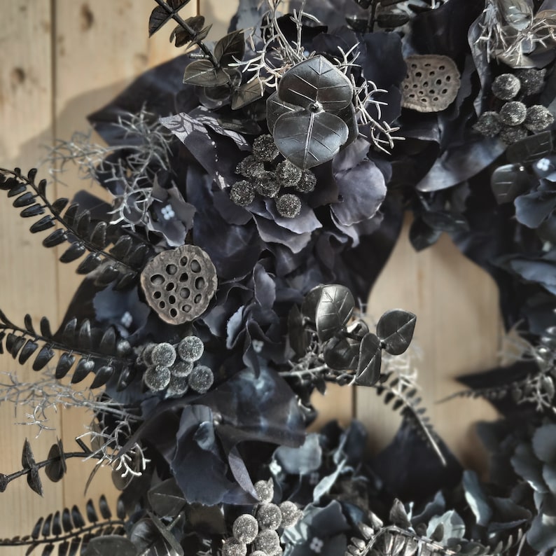 May include: A black and gray wreath with various floral elements, including hydrangeas, eucalyptus, and lotus pods.