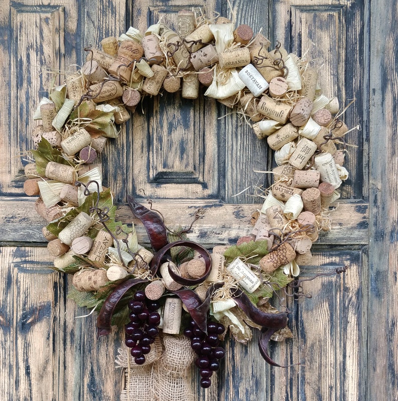 May include: A rustic wreath made of cork and twine, decorated with dried leaves and grapes. The wreath features several wine cork labels with names like "Oregonian" and "Bugatti".