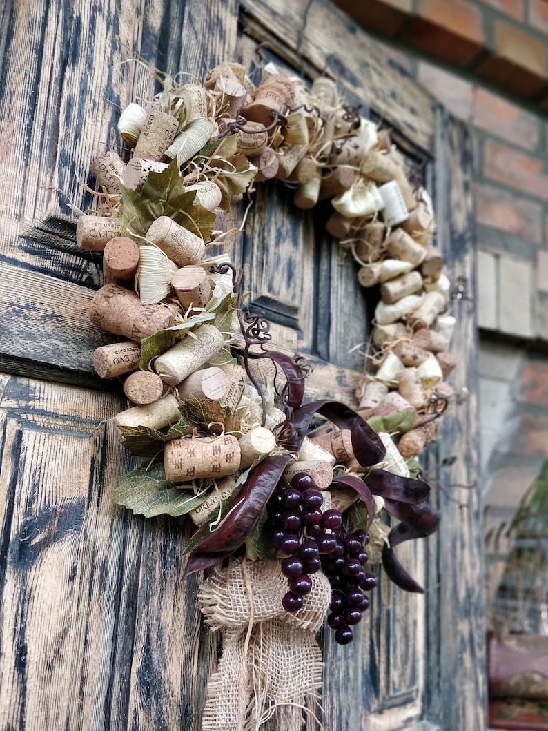 May include: A rustic wreath made of wine corks, burlap, and grape clusters. The wreath is decorated with dried leaves and is hanging on a wooden door.