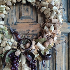 May include: A rustic wine cork wreath with faux grapes and burlap accents. The wreath is decorated with wine corks with various labels, including "OREANDA", "BOSTAVAN", "KOBLEVO", and "BUGULMA".