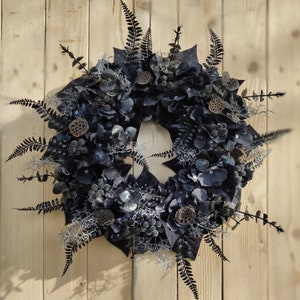 May include: A black and gray wreath made of dried flowers, leaves, and branches. The wreath is decorated with small, dried lotus pods.