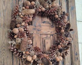 May include: A brown, rustic-style wreath made of pine cones, acorns, and other natural elements. The wreath is hanging on a wooden door.