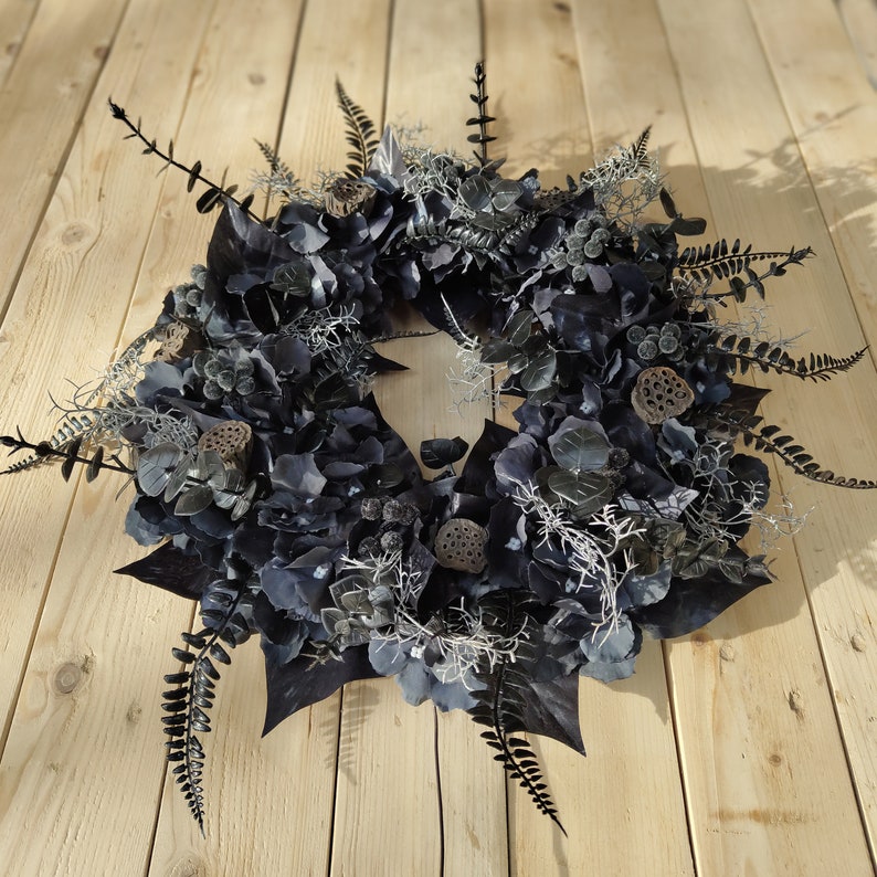 May include: A black and silver wreath made of dried hydrangeas, ferns, and lotus pods.