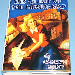 May include: A vintage hardcover book titled "Nancy Drew Mystery Stories: The Quest of the Missing Map" by Carolyn Keene. The cover art features a woman in a red top and blue skirt, holding a map near a piano.
