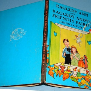 May include: A vintage children's book titled "Raggedy Ann and Raggedy Andy's Friendly Fairies" by Johnny Gruelle. The cover is a vibrant blue with a colorful illustration of the characters and fairies. The book's spine is visible, showing the title.