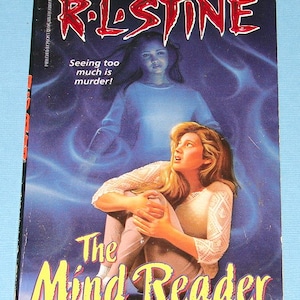 May include: A paperback book cover for "The Mind Reader" by R.L. Stine. The cover features a woman looking up in fear, with a ghostly figure behind her. Text includes "FEAR STREET" and "Seeing too much is murder!"