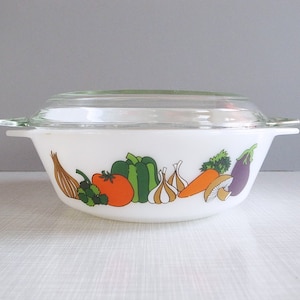 May include: White ceramic casserole dish with a glass lid. The dish has a colorful vegetable design featuring a tomato, onion, garlic, pepper, carrot, mushroom, and eggplant.