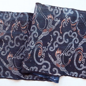 May include: A dark blue fabric with a repeating pattern of white cranes flying in a swirling, white cloud design. The cranes have orange accents.