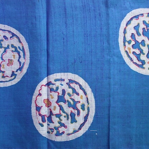 May include: A blue textile with a repeating pattern of white circles. Each circle contains a floral design with red, blue, and yellow accents. The fabric has a textured appearance.