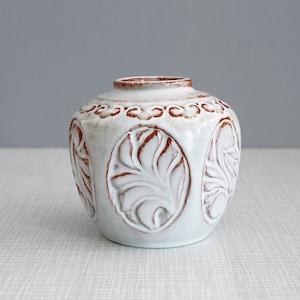 Könnte beinhalten: Weiße Keramikvase mit brauner Glasur und geprägtem Blattdesign.