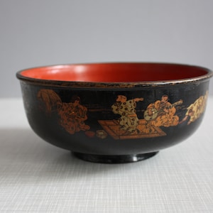 May include: A black lacquer bowl with a red interior and gold painted figures playing a game. The bowl is a traditional Japanese design.