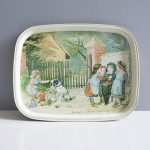 Pode incluir: Uma bandeja de metal vintage com uma ilustração colorida de crianças brincando com um cachorro em frente a uma casa. A bandeja tem um fundo branco e uma borda elevada.