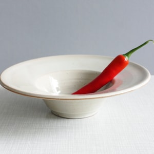 以下が含まれることがあります： 縁が広く、中央が深い白い陶器のボウル。中に赤い唐辛子が置かれている。