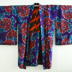 Op de afbeelding: Een paarse en blauwe kimono met een rood en oranje bloemenpatroon. De kimono is gemaakt van zijde en heeft een traditioneel Japans ontwerp.