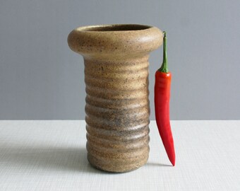 Może przedstawiać: Brązowy ceramiczny wazon z żebrowaną fakturą i szeroką, zaokrągloną górą. Czerwona papryczka chili stoi prosto obok wazonu.
