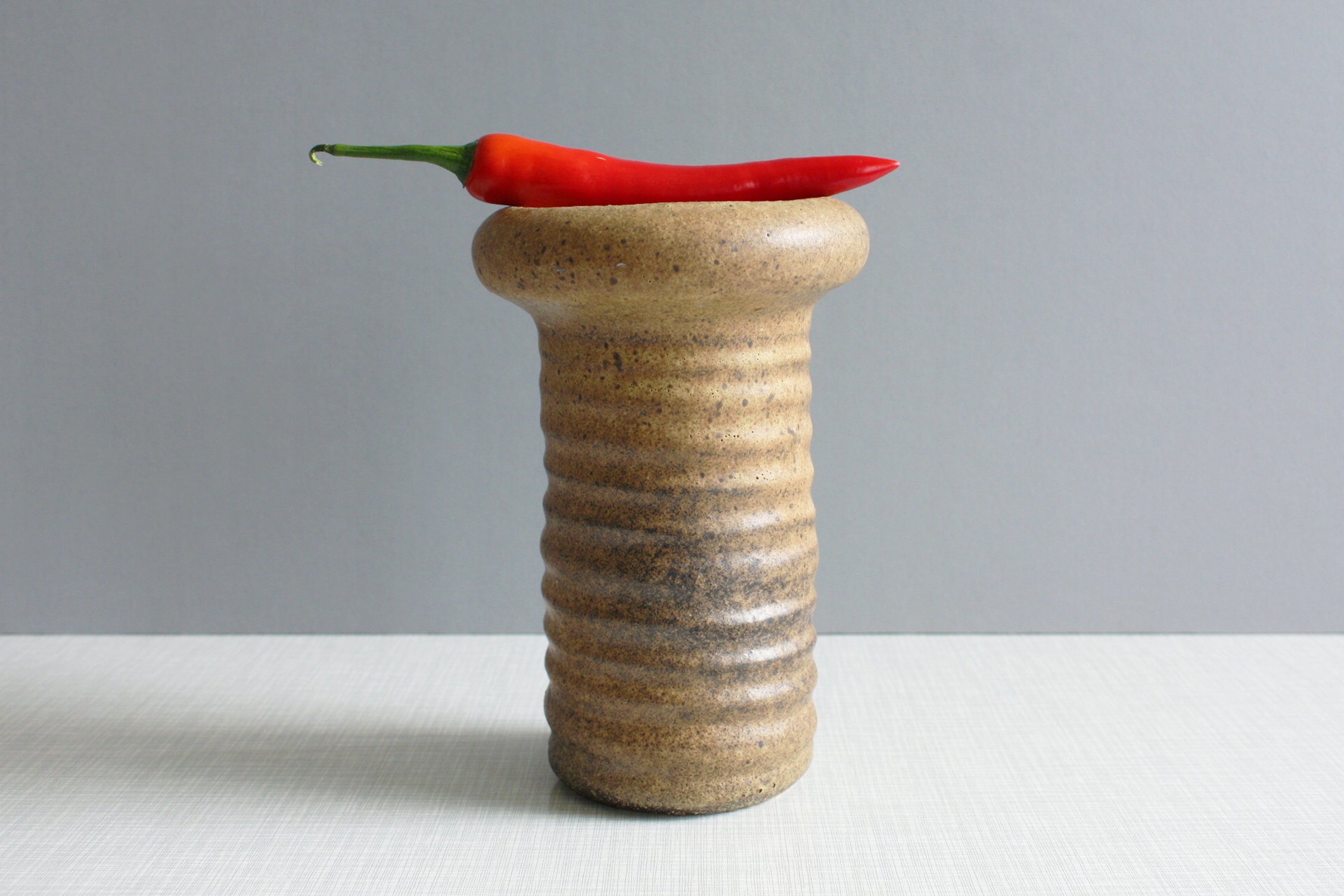 Puede incluir: Un jarr&oacute;n de cer&aacute;mica marr&oacute;n con una superficie texturizada y acanalada. Un chile rojo descansa sobre la parte superior del jarr&oacute;n.