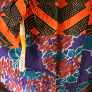 Op de afbeelding: Een close-up van een kleurrijke stof met een geometrisch patroon in zwart en oranje en een bloemenpatroon in paars, blauw en rood.