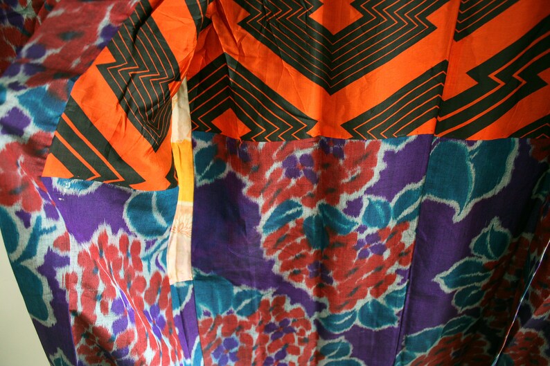 Op de afbeelding: Een close-up van een kleurrijke stof met een geometrisch patroon in zwart en oranje en een bloemenpatroon in paars, blauw en rood.
