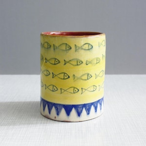 May include: A yellow ceramic mug with a blue and white trim. The mug is decorated with a pattern of blue fish.